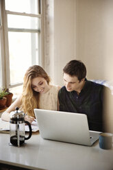 Smiling couple looking down while sitting with laptop computer at home - CAVF02099