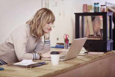 Woman with hand on chin using laptop computer in shop - CAVF02151