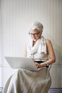 Ältere Frau benutzt einen Laptop, während sie auf einem Stuhl in einem Geschäft sitzt - CAVF02177