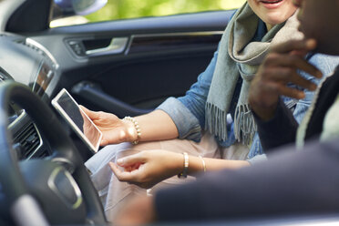 Frau zeigt Mann Tablet-Computer, während sie im Auto sitzt - CAVF02180