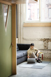 Businessman using laptop computer while sitting on floor in office - CAVF02212