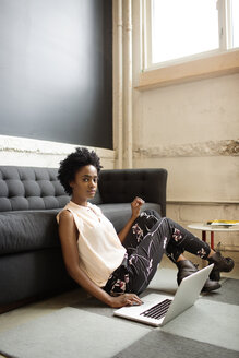 Porträt einer Frau, die einen Laptop benutzt, während sie im Büro auf dem Boden sitzt - CAVF02214