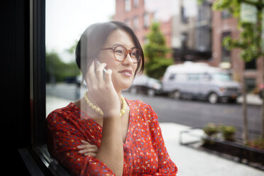 Glückliche Frau, die am Fenster stehend mit ihrem Smartphone spricht - CAVF02217