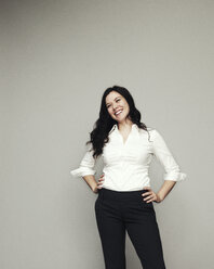 Happy woman with hands on hip standing against gray background - CAVF02241