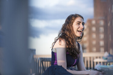 Cheerful woman laughing while sitting on chair against sky - CAVF02247