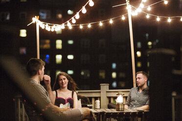 Freunde unterhalten sich nachts auf der Terrasse eines Gebäudes - CAVF02265