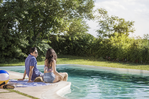 Paar im Gespräch am Pool sitzend, lizenzfreies Stockfoto