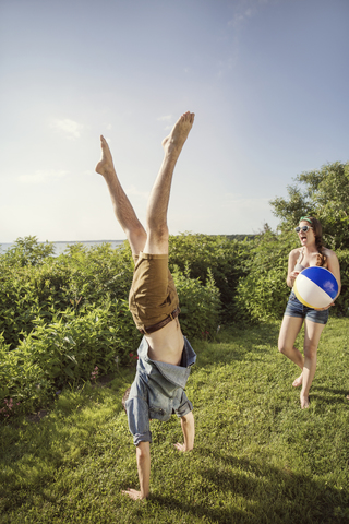 Fröhliche Frau schaut auf einen Mann, der im Hinterhof einen Handstand macht, lizenzfreies Stockfoto