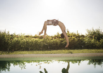 Mann springt mit einem Salto ins Schwimmbad gegen den klaren Himmel - CAVF02288