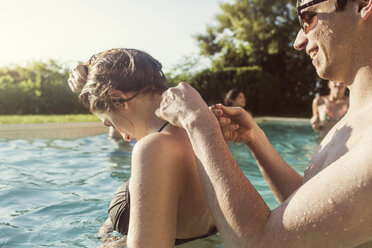 Happy man tying woman's bikini top while enjoying in pool - CAVF02293