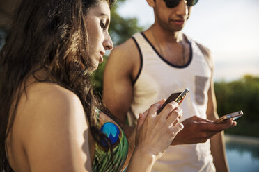 Ein Paar benutzt ein Mobiltelefon, während es am Pool steht - CAVF02310