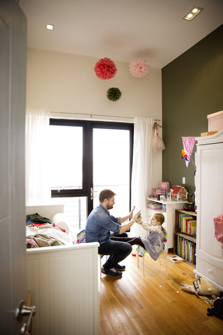 Seitenansicht von Vater und Tochter, die auf einem Stuhl sitzend zu Hause spielen, lizenzfreies Stockfoto