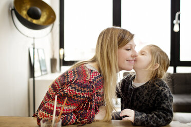 Mädchen küsst Mutter, während sie zu Hause am Tisch sitzt - CAVF02441