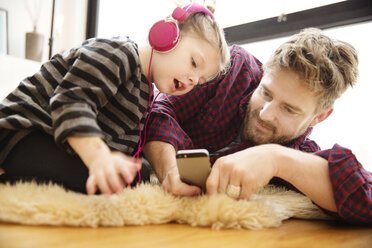 Vater und Tochter schauen auf ihr Handy, während sie zu Hause auf dem Boden liegen - CAVF02451