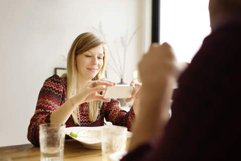 Frau benutzt Mobiltelefon, während sie neben einem Mann am Esstisch sitzt, lizenzfreies Stockfoto