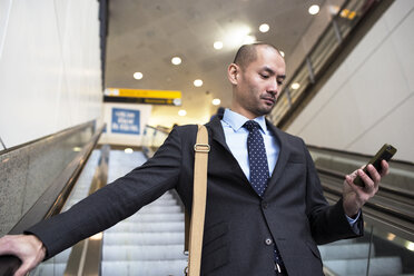 Geschäftsmann, der ein Mobiltelefon benutzt, während er auf einer Rolltreppe in einer U-Bahn-Station steht - CAVF02479