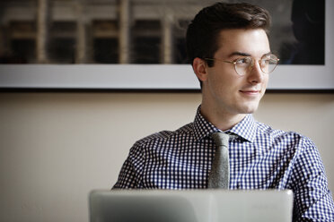 Man looking away while sitting with laptop computer at home - CAVF02487