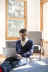 Mann, der einen Laptop benutzt, während er zu Hause sitzt - CAVF02509