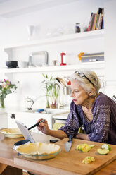 Frau benutzt Tablet-Computer beim Backen von Apfelkuchen in der Küche - CAVF02535