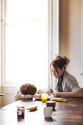 Mutter unterrichtet ihren Sohn, während sie zu Hause am Tisch sitzt - CAVF02553