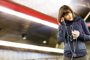 Frau hört Musik, während sie in einer U-Bahn-Station steht - CAVF02564