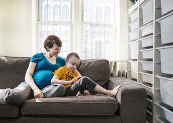 Pregnant woman with son sitting on sofa at home - CAVF02588