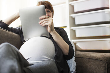 Schwangere Frau benutzt Tablet-Computer, während sie sich zu Hause auf dem Sofa entspannt - CAVF02603