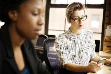 Businesswoman using smart phone while working with colleague in office - CAVF02620