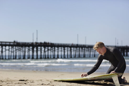 Mann bereitet sich auf das Surfen vor, während er am Strand kniet - CAVF02644
