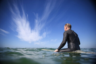 Rückansicht eines Mannes, der auf einem Surfbrett im Meer sitzt, gegen den Himmel - CAVF02648