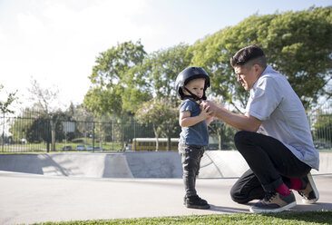Seitenansicht eines Vaters, der seinem Sohn in einem Skateboardpark beim Tragen eines Helms hilft - CAVF02661