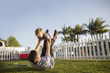 Vater spielt mit seinem Sohn, während er im Hinterhof im Gras liegt - CAVF02664