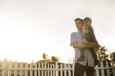 Father carrying son while standing at backyard against clear sky - CAVF02666