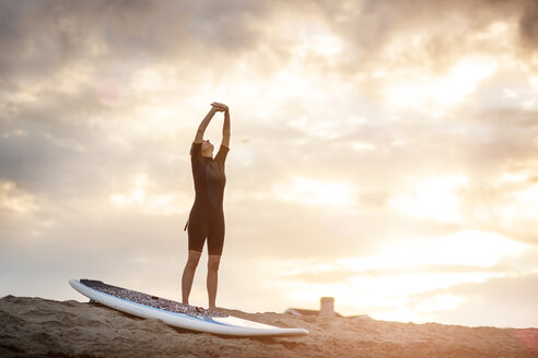 Frau, die sich mit einem Paddleboard am Strand bei Sonnenuntergang dehnt - CAVF02668