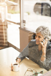 Happy woman talking on mobile phone while sitting at cafe - CAVF02681