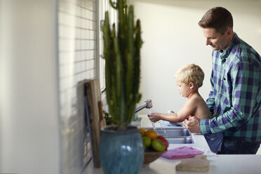 Father assisting son in washing hand at sink in kitchen - CAVF02697