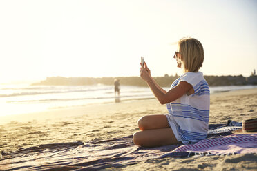Seitenansicht einer Frau, die am Strand sitzend fotografiert - CAVF02706