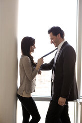 Cheerful couple standing against glass window - CAVF02849