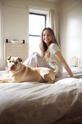 Porträt einer glücklichen Frau mit Hund auf dem Bett, lizenzfreies Stockfoto