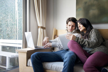 Frau zeigt ihrem Freund auf dem Sofa zu Hause ein digitales Tablet - CAVF02906