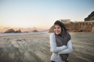 Young woman standing on beach with arms crossed against sky - CAVF02926