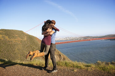 Junges Paar umarmt sich auf dem Feld vor der Golden Gate Bridge - CAVF02928