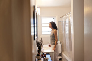Glückliche Frau steht am Waschbecken im Badezimmer - CAVF02934