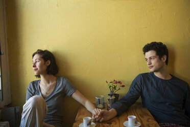 Lächelndes Paar, das sich am Tisch an der Wand an den Händen hält - CAVF02953