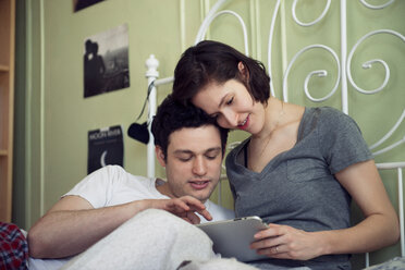 Glückliches Paar betrachtet digitales Tablet auf dem Bett zu Hause - CAVF02954