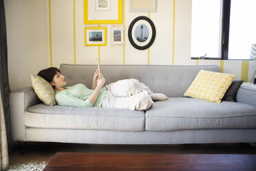 Frau benutzt Tablet-Computer, während sie zu Hause auf dem Sofa liegt - CAVF02967