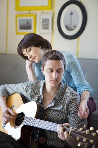 Frau hört ihrem Freund zu, der zu Hause Gitarre spielt, lizenzfreies Stockfoto