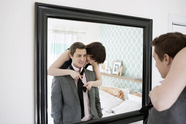 Smiling woman tying boyfriend's necktie in front of mirror - CAVF02972