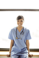Porträt einer lächelnden Ärztin auf dem Fensterbrett sitzend - CAVF02994