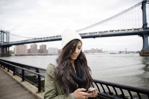 Frau benutzt Telefon, während sie auf der Promenade vor der Manhattan-Brücke in der Stadt steht - CAVF02998